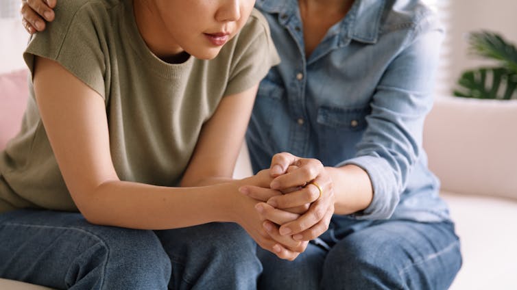 A young woman being comforted by an older woman, sitting on a couch